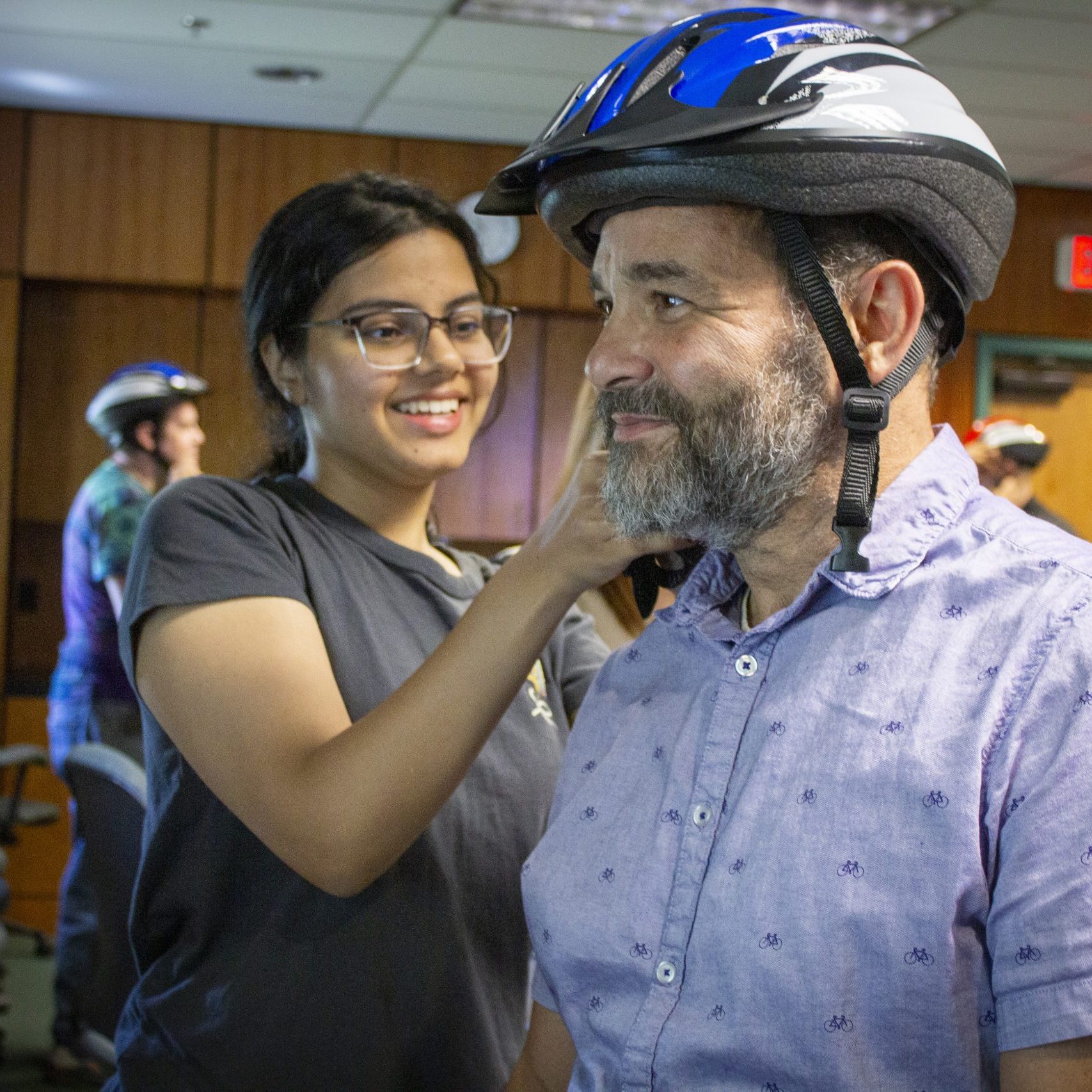 Female student practices fitting a bicycle helmet on an adult male. Her hands are adjusting the helmet straps of the helmet on his head.