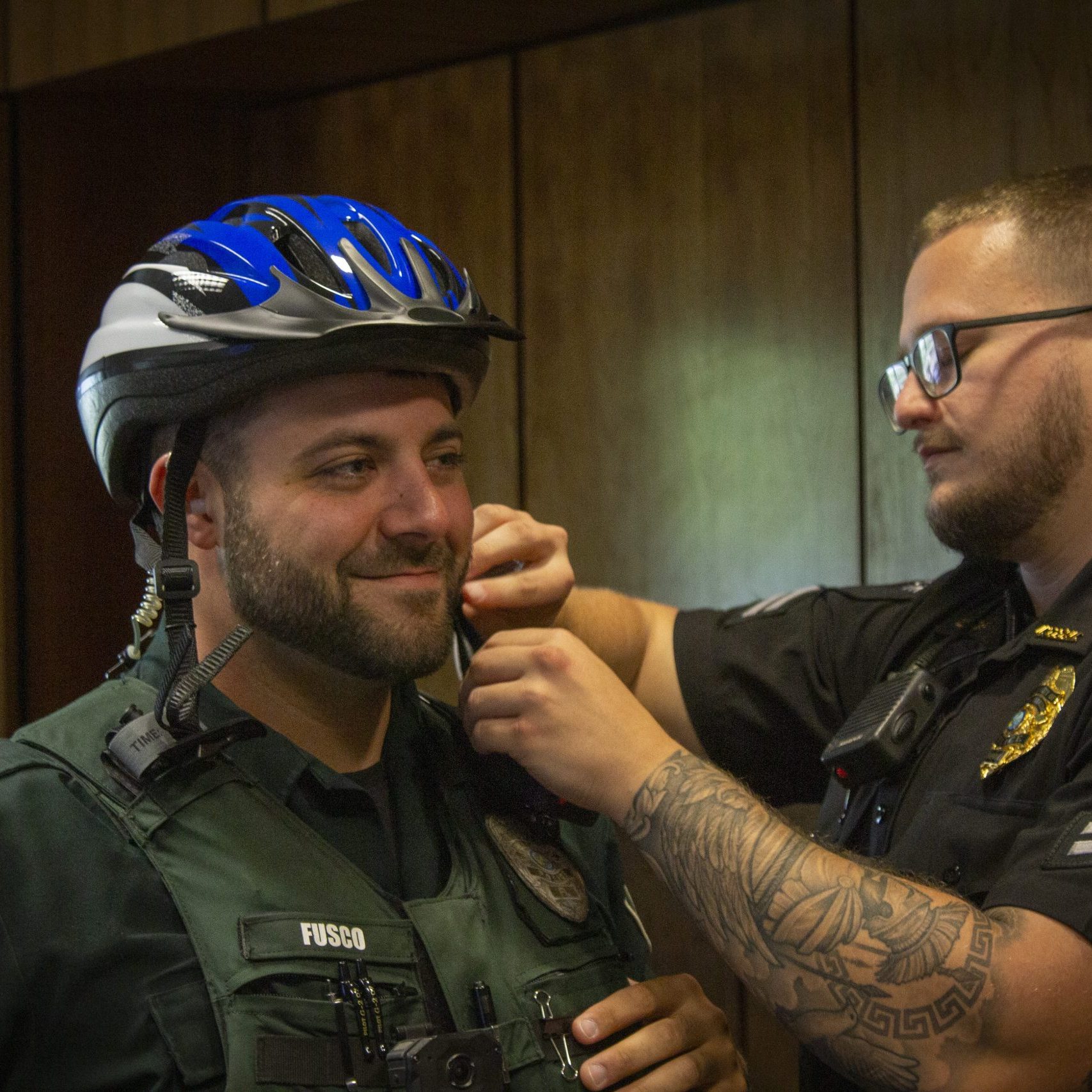 An adule male police officer adjust a helmet strap on another male police officer.