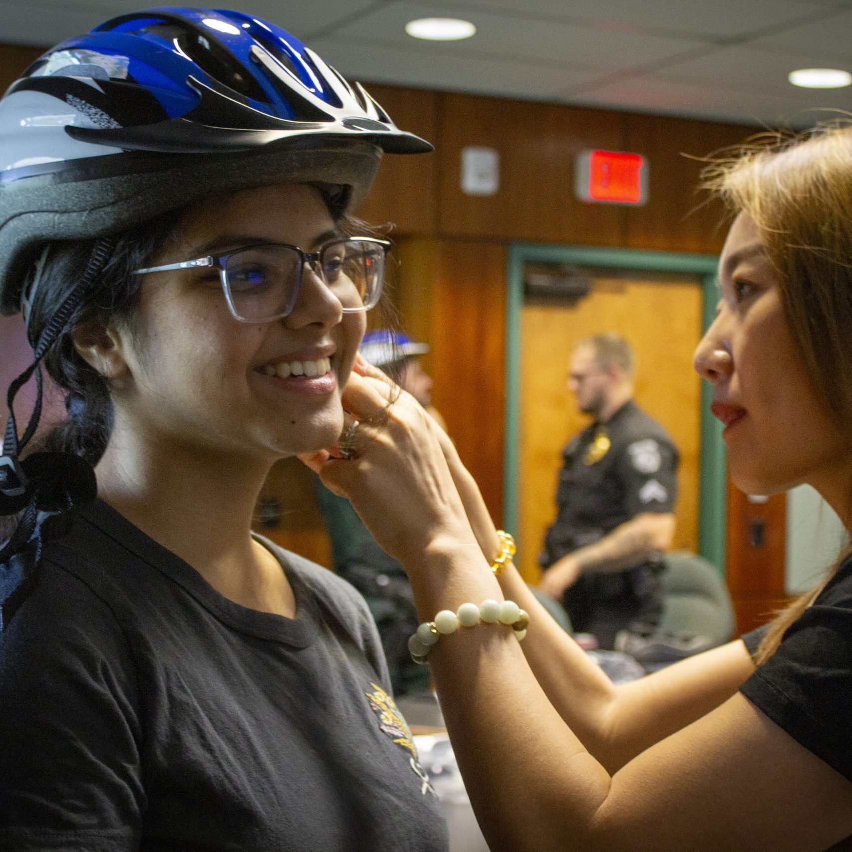An adult female adjusts a helmet strap on a female student.