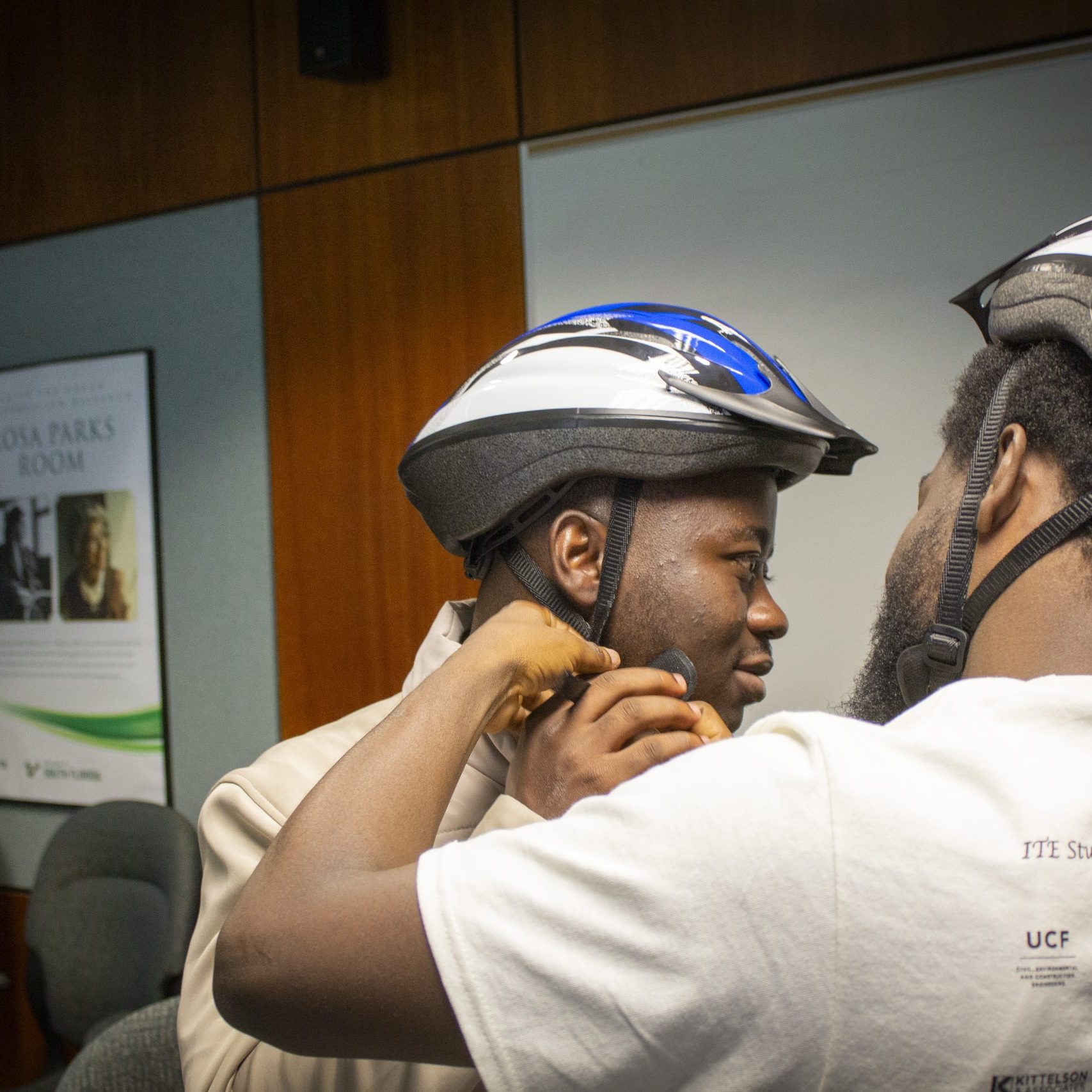 One male student adjusts the helmet strap on another male student.