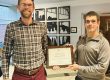 Two men standing next to each other holding a certificate together.