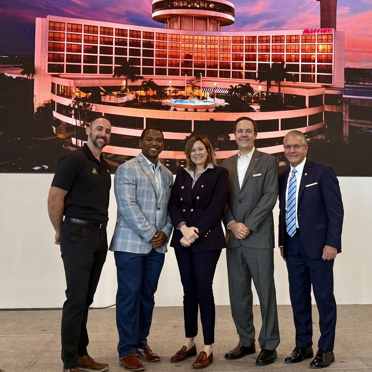 Group of adults stands in front of photo of airport hotel.