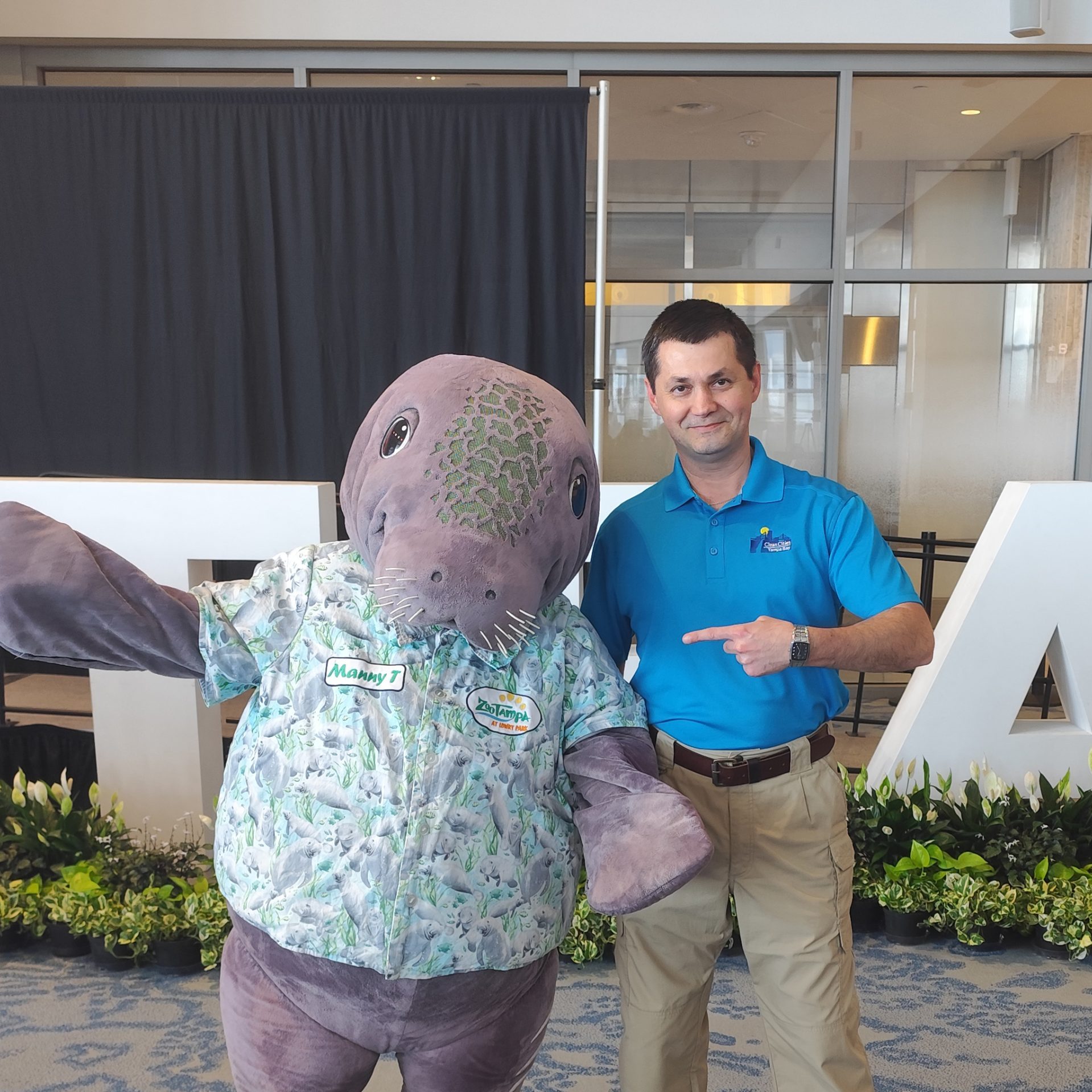 man stands next to person in manatee mascot costume