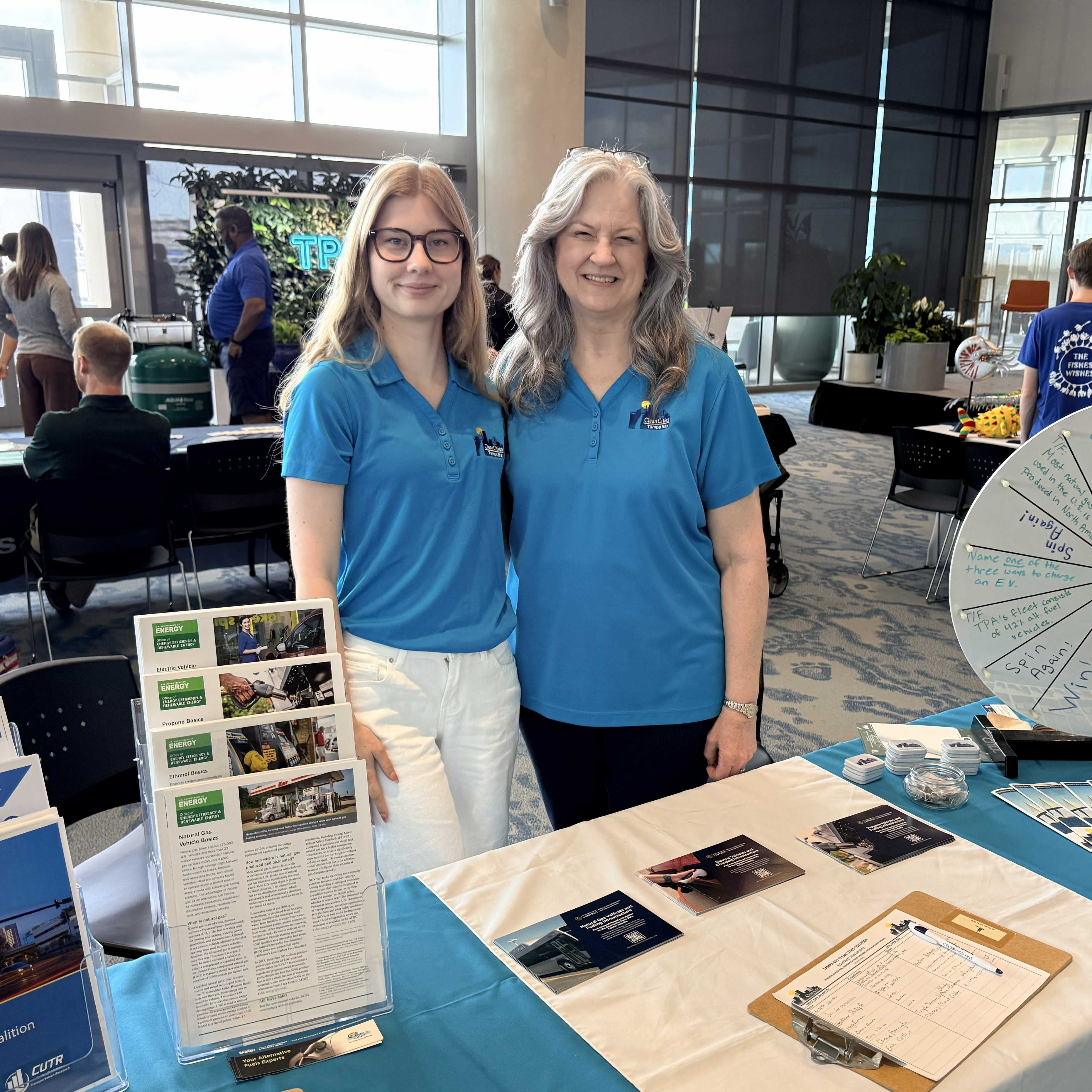 Two women stand next to exhibitor table displaying informational materials.