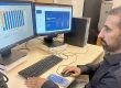 Adult male sits in from of a computer with two monitors, looking at data graphs.